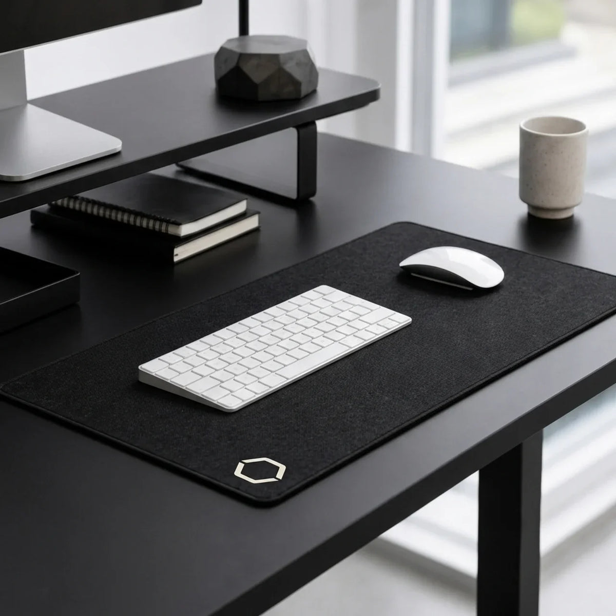 The Difavo Desk Mat on a black desk with a monitor riser, a notebook and a mug