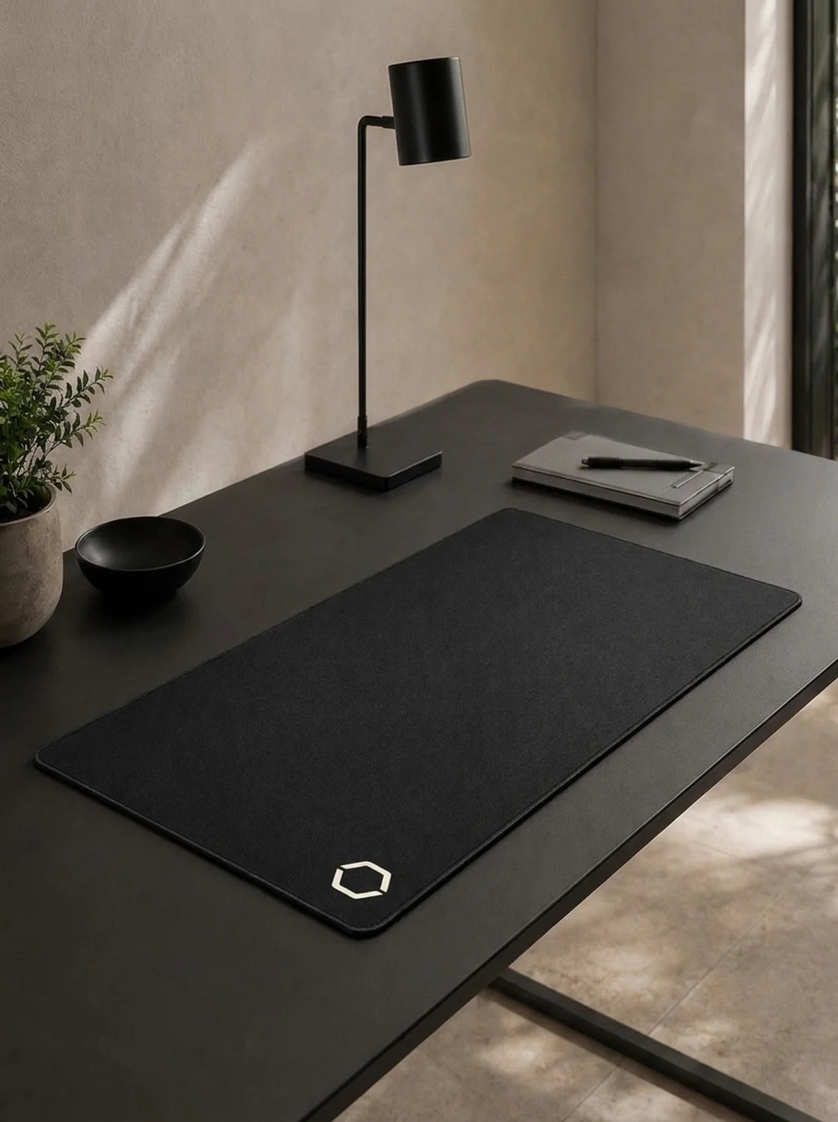 A quiet black desk with the Difavo Desk Mat, a task lamp and a notebook